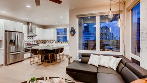 A modern kitchen with stainless steel appliances, a dining area with bar stools, and a large window offering a view of the city. - Old Town Swank - Brand New To Brewery District! (Fort Collins)