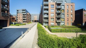 Et moderne lejlighedskompleks i byen med flere etager, altaner og en belagt sti.