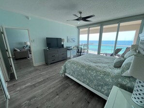 Et soveværelse med en stor seng, en kommode, et fjernsyn og en balkon med udsigt over havet.
