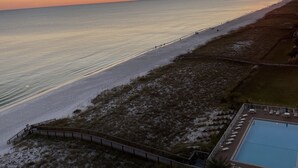 Une vue sur la plage avec un coucher de soleil, une piscine et une promenade en bord de mer.