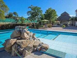 A swimming pool with a rock formation, surrounded by palm trees and a thatched-roof structure. - Hotel Parotas Manzanillo (Manzanillo)