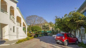 A building with a white facade, arched windows, and a red car parked in front. - Hotel Parotas Manzanillo (Manzanillo)