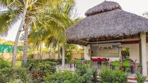 A thatched-roof outdoor dining area with multiple tables and chairs, surrounded by lush greenery and palm trees. - Hotel Parotas Manzanillo (Manzanillo)