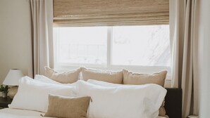 A neatly made bed with multiple pillows, a bedside lamp, and a window with a wooden blind. - *Great Rates Available* | Cactus Rose (Scottsdale)