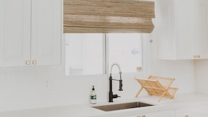 A kitchen with white cabinetry, a window with a wooden blind, a black faucet, a bottle of dish soap, and a wooden chair. - *Great Rates Available* | Cactus Rose (Scottsdale)