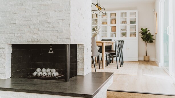 A modern kitchen with a white brick wall, a black countertop, and a fireplace with a hanging light fixture. - *Great Rates Available* | Cactus Rose (Scottsdale)