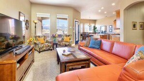 A spacious living room with a large flat-screen TV, a leather sofa, and a coffee table. There are two patterned armchairs and a dining area in the background. - Upscale with Mtn Views, Hot Tub, 25 Mins to Zion NP (La Verkin)