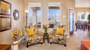 A living room with two patterned armchairs, a small table with a vase of flowers, and a view of mountains through large windows. - Upscale with Mtn Views, Hot Tub, 25 Mins to Zion NP (La Verkin)