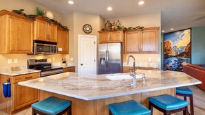 A kitchen with wooden cabinets, a stainless steel refrigerator, a microwave, and a large island with bar stools. - Upscale with Mtn Views, Hot Tub, 25 Mins to Zion NP (La Verkin)