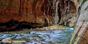 Un canyon étroit, traversé par une rivière, avec un terrain rocheux et une personne se tenant au loin.