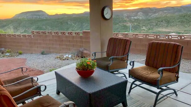 An outdoor patio with wicker furniture, a clock, and a view of a mountainous landscape during sunset. - Upscale with Mtn Views, Hot Tub, 25 Mins to Zion NP (La Verkin)