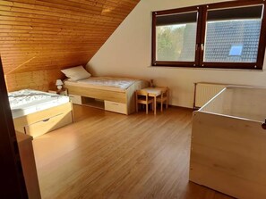 Una camera da letto con soffitto spiovente, pavimento in legno, un letto, un tavolino e una finestra.