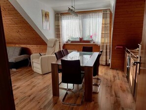 Ein Essbereich mit Holztisch und Stühlen, einer Couch und einem Fenster mit Vorhängen.