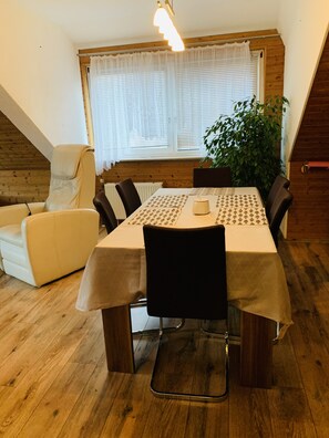 Zona pranzo con tavolo apparecchiato per quattro, circondato da sedie, un termosifone e una finestra con persiane.