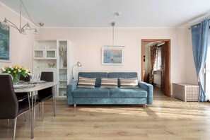 A living room with a sofa, dining table, and chairs. There is a bookshelf and a painting on the wall.