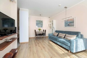 A modern living room with a blue sofa, wooden flooring, and a dining area with a table and chairs.