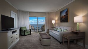 A hotel room with a flat-screen TV, a green armchair, a grey sofa with patterned cushions, a small table, and a view of the ocean through large windows. - Marriott's OceanWatch Two Bedroom Beachfront Resort (Myrtle Beach)
