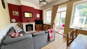 A living room with a grey sofa, a fireplace, a television, and a dining table. - Cosy traditional cottage with parking and garden (Ryde)