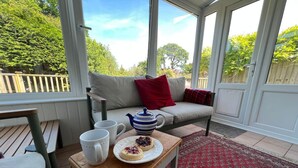 A conservatory with a wooden table, a sofa, and a red patterned rug. - Cosy traditional cottage with parking and garden (Ryde)