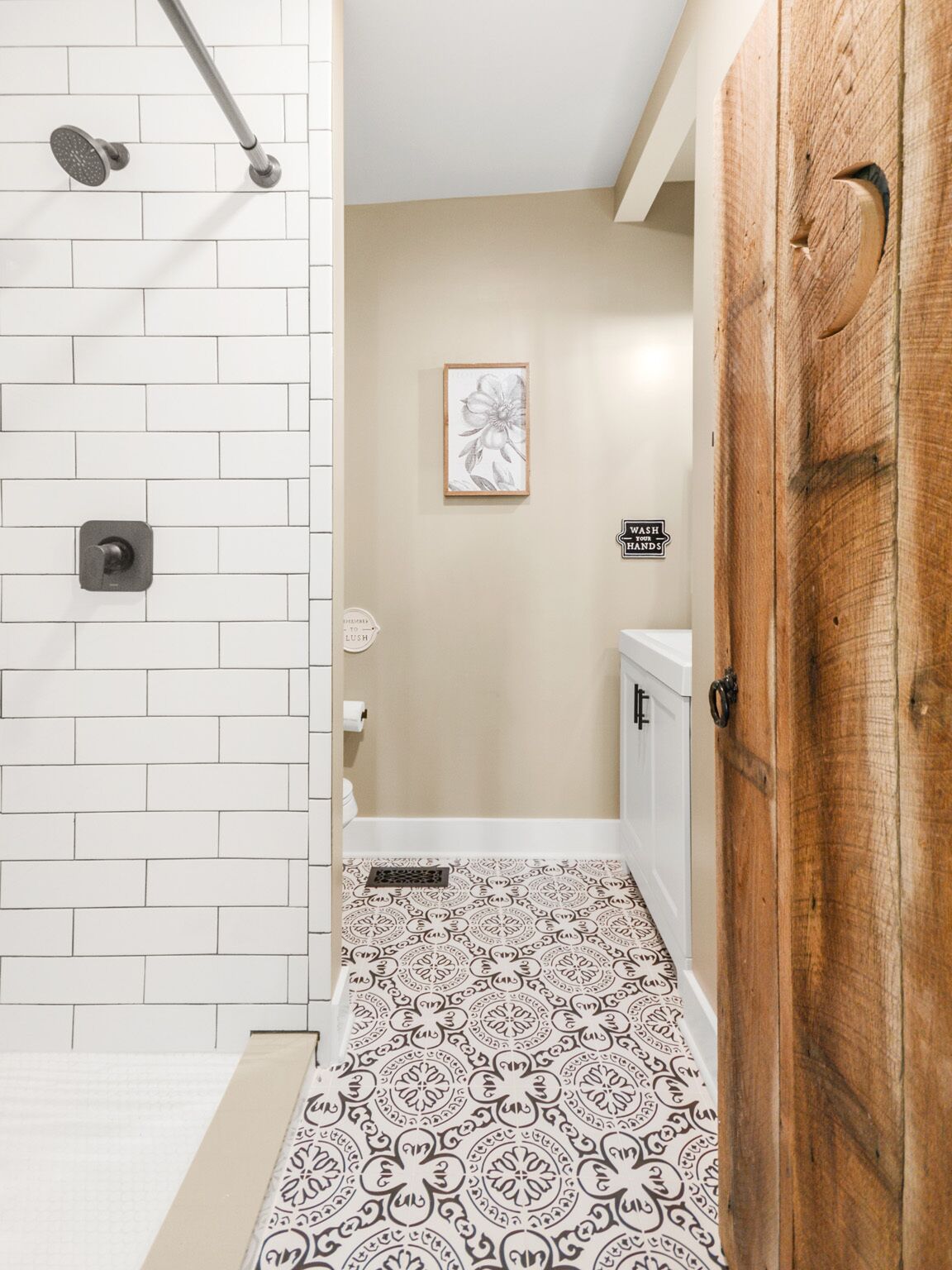 Une salle de bain équipée d’une douche, de toilettes et d’un lavabo, avec des carreaux blancs et un carrelage au motif décoratif.