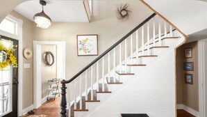 A staircase with white railings and wooden steps, leading to a door with a wreath and a framed picture on the wall. - Welcome to the Rusty Rose-Restored Farmhouse feel in the heart of Jefferson, MD (Jefferson)