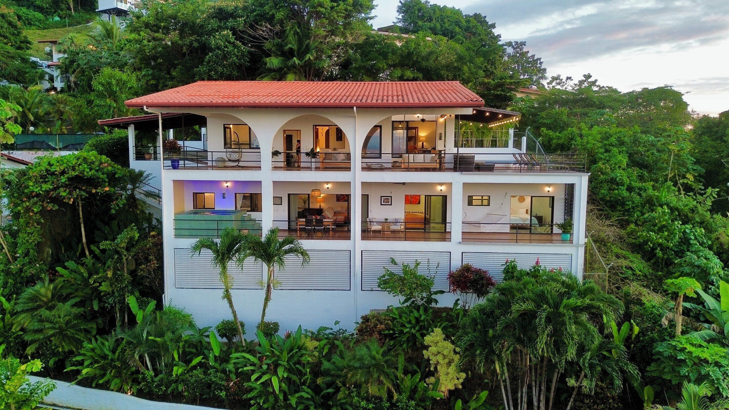 A multi-story building with a red-tiled roof, balconies, and a pool.