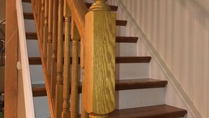 Eine Holztreppe mit Handlauf und einer weißen Wand mit vertikalen Jalousien.