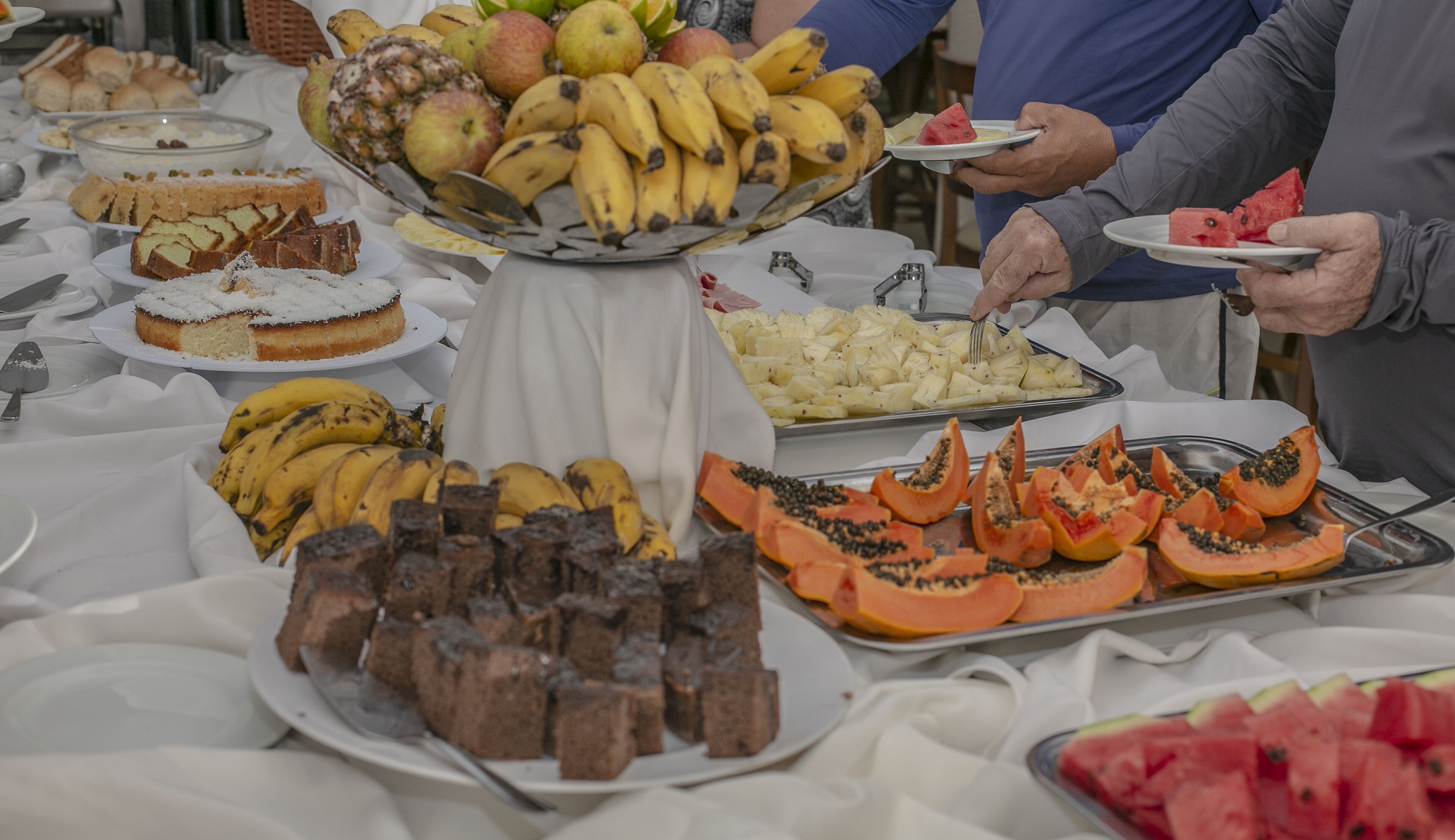 A buffet table with various food items including fruits, cakes, and desserts.