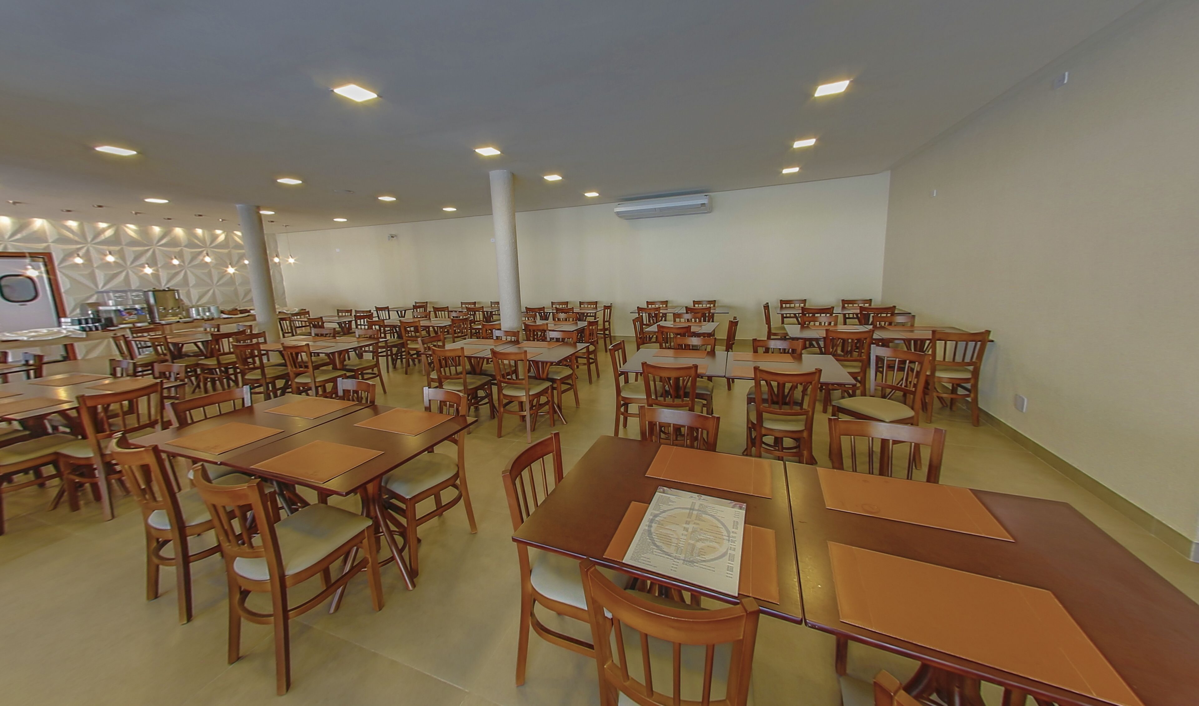 A large dining hall with multiple wooden tables and chairs, arranged in rows.
