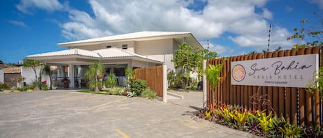 A modern hotel with a covered entrance, a signboard, and a landscaped garden area.