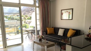 Uma sala de estar moderna com sofá, mesa de centro e vista para uma varanda com mobiliário externo.