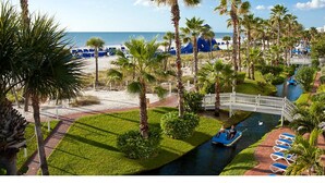 A resort with a pool, palm trees, and a bridge over a water channel.