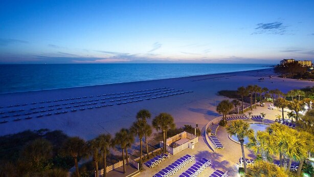 A beach resort with sun loungers, a pool, and a view of the ocean.