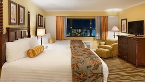 A hotel room with a large bed, a sofa, a chair, a TV, and a view of the city at night.