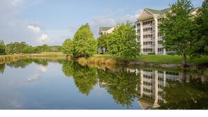 A hotel with a reflection in a calm lake, surrounded by greenery and a clear sky. - GRANDE VILLAS AT WORLD GOLF VILLAGE (St. Augustine)