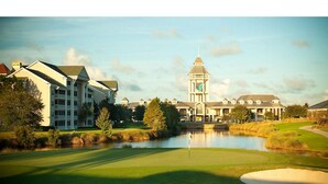 A golf course with a pond, surrounded by buildings with a clock tower. - GRANDE VILLAS AT WORLD GOLF VILLAGE (St. Augustine)