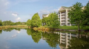 Um hotel refletido em um lago calmo, cercado por vegetação e céu claro.