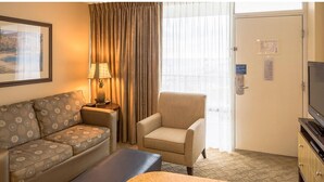 Hotelkamer met een bank, fauteuil, tv-meubel en een deur met een bordje.