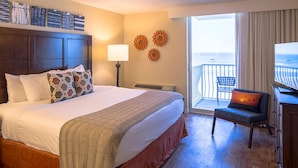 A hotel room with a large bed, a desk with a chair, a balcony with a view, and decorative wall art. - CASA DEL MAR BEACH RESORT (Ormond Beach)