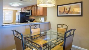 Una cocina moderna con armarios de madera, un refrigerador de acero inoxidable y una mesa de comedor de vidrio con cuatro sillas.