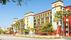 Un hotel de varios pisos con un patio central, palmeras y un estacionamiento.