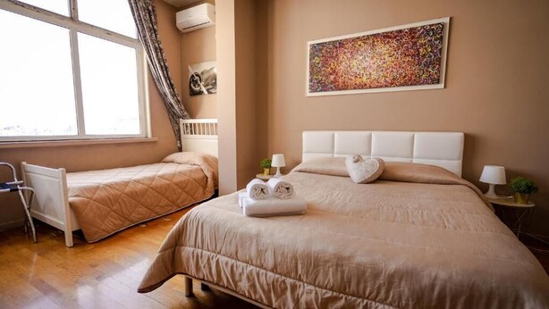 A hotel room with two beds, a window, a radiator, a painting, and a bedside table with a lamp. - Dolci Emozioni Room 82 (Bari)