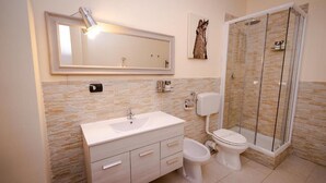 A bathroom with a stone-tiled wall, a white sink, a toilet, and a glass-enclosed shower. - Dolci Emozioni Room 82 (Bari)
