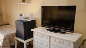 Una habitación de hotel con una cama, un aparador blanco con cajones, un televisor negro encima y un refrigerador pequeño.