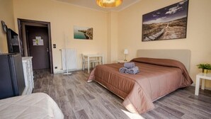 Una habitación de hotel con cama, escritorio, silla, radiador y un cuadro en la pared.