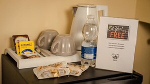 Preparación para el desayuno en una habitación de hotel, que incluye una cafetera, tazas, una botella de agua, un paquete de café Bonomelli y un letrero que dice 'It's Free'.