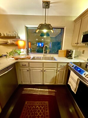 A modern kitchen with white cabinets, a stainless steel sink, a built-in oven, and a window above the sink. - Secluded Tree House Chalet (Issaquah)