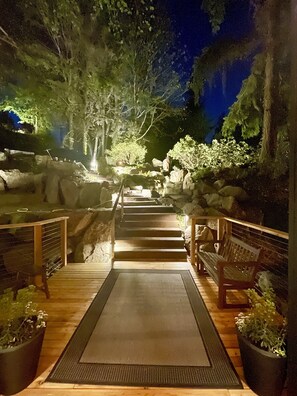 A wooden pathway leading to a seating area with benches, surrounded by rocks and plants, under night lighting. - Secluded Tree House Chalet (Issaquah)