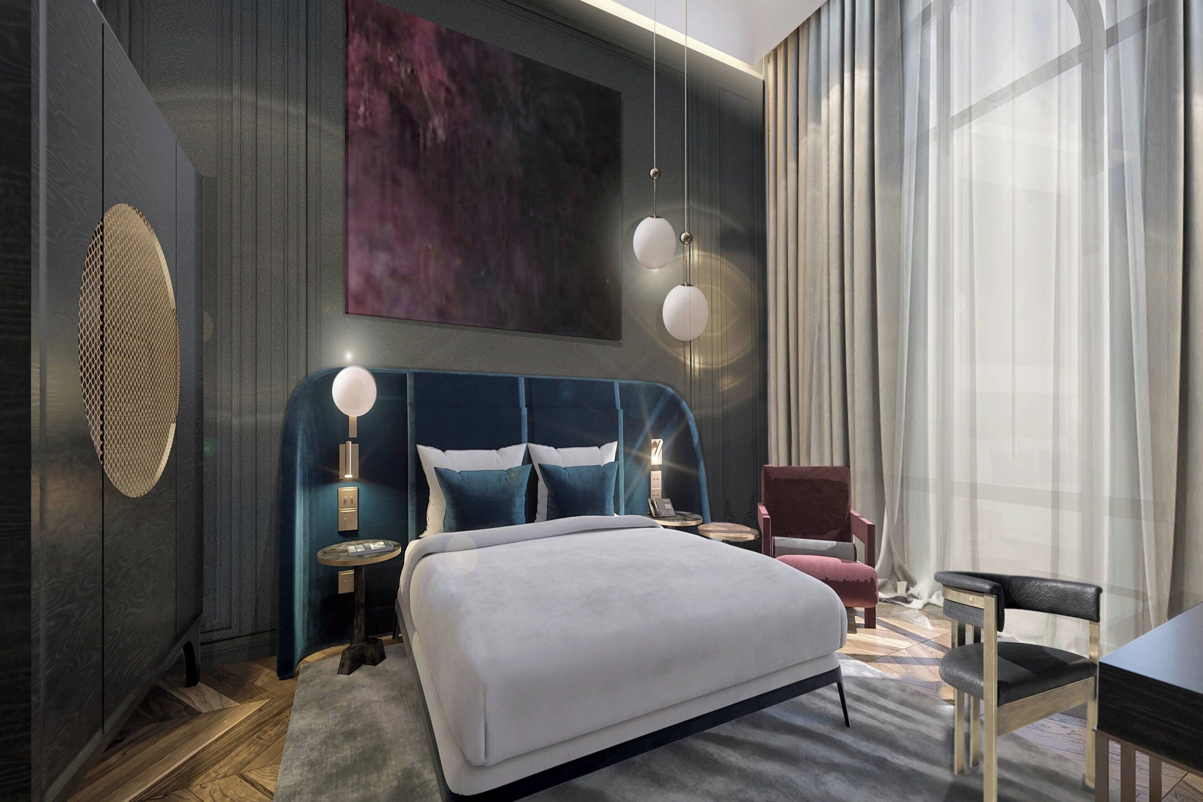 A modern hotel room with a large bed, a round bedside table, a chair, and a desk.