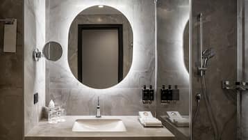 A modern bathroom with a large oval mirror, a sink, and a shower.